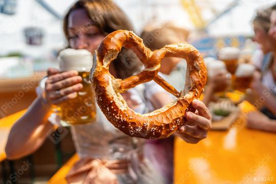 Woman holding a giant pretzel and drinking beer out of a mug with people talking and drinking beer in the background at oktoberfest in munich or  dult in germany  : Stock Photo or Stock Video Download rcfotostock photos, images and assets rcfotostock | RC Photo Stock.: