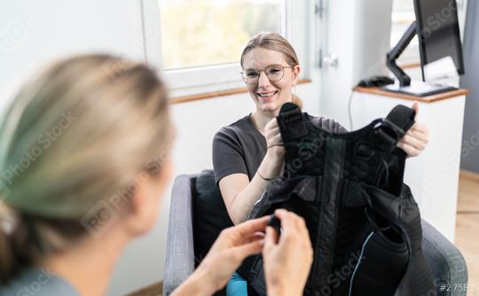 woman holding an EMS training vest explaining by talking to a trainer in a consultation room in a EMS - Studio  : Stock Photo or Stock Video Download rcfotostock photos, images and assets rcfotostock | RC Photo Stock.: