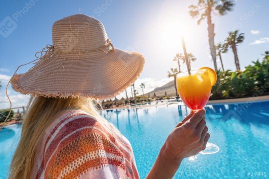 Woman in a straw hat holding a colorful cocktail by a pool with palm trees and sunlight in the background  at caribbean island hotel   : Stock Photo or Stock Video Download rcfotostock photos, images and assets rcfotostock | RC Photo Stock.: