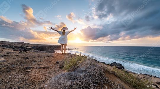 Woman in a white dress and sun hat with arms raised facing the sea on sunset at Playa de Cofete, Fuerteventura, Canary Islands.  : Stock Photo or Stock Video Download rcfotostock photos, images and assets rcfotostock | RC Photo Stock.: