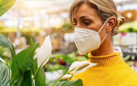 woman in a yellow sweater wearing a white face mask stands amidst lush greenery, appreciating a white flower, with a softly lit store backdrop. Shopping in a greenhouse or garden center concept image  : Stock Photo or Stock Video Download rcfotostock photos, images and assets rcfotostock | RC Photo Stock.: