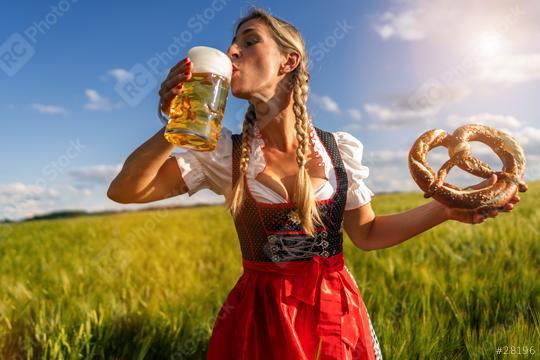 Woman in Bavarian dress drinking beer and holding a pretzel in a sunny wheat field at Oktoberfest in munich  : Stock Photo or Stock Video Download rcfotostock photos, images and assets rcfotostock | RC Photo Stock.: