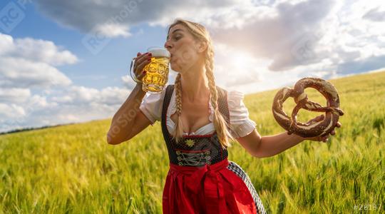 Woman in Bavarian tracht drinking beer and holding a big pretzel in a wheat field at sunset celebrating Oktoberfest festival in munich.  : Stock Photo or Stock Video Download rcfotostock photos, images and assets rcfotostock | RC Photo Stock.: