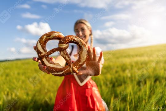 Woman in Bavarian tracht playfully holding a pretzel in a field, with focus on the pretzel ready for Oktoberfest or dult festival in munich.  : Stock Photo or Stock Video Download rcfotostock photos, images and assets rcfotostock | RC Photo Stock.: