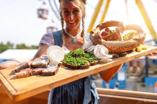 woman in Bavarian tracht presenting traditional German snacks (pretzel, sliced bread, radishes) at a vibrant fairground dult or oktoberfest in germany  : Stock Photo or Stock Video Download rcfotostock photos, images and assets rcfotostock | RC Photo Stock.: