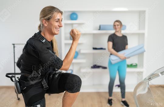 Woman in EMS suit doing squats with trainer holding yoga mat for the next training exercise in a EMS studio  : Stock Photo or Stock Video Download rcfotostock photos, images and assets rcfotostock | RC Photo Stock.: