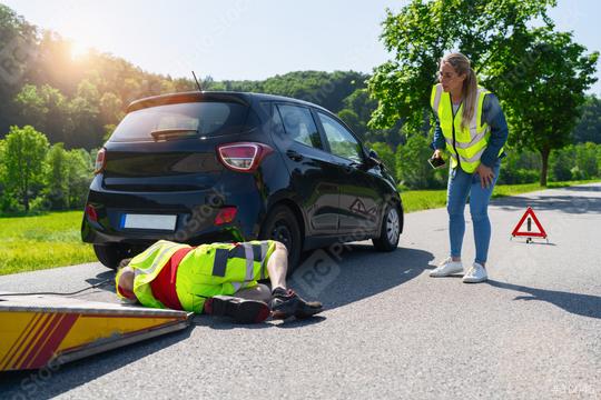 Woman in life jacket stands at her accident car and watches skeptically as a towing service employee attaches a tow rope to her car to tow it away, with a warning triangle in the background.  : Stock Photo or Stock Video Download rcfotostock photos, images and assets rcfotostock | RC Photo Stock.: