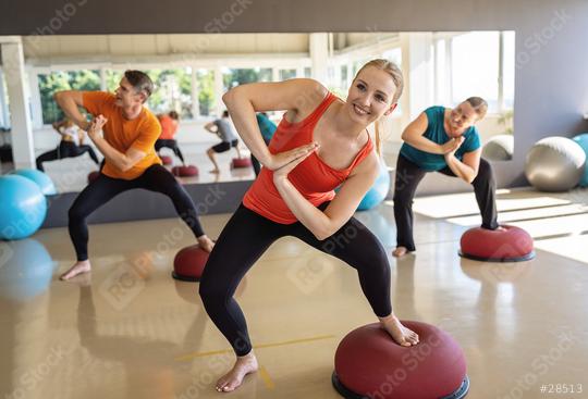 Woman in orange top doing a twist on a Bosu Ball with fitness class behind her  : Stock Photo or Stock Video Download rcfotostock photos, images and assets rcfotostock | RC Photo Stock.: