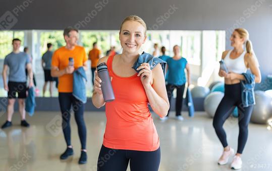 Woman in orange top holding a water bottle in a gym with other people in the background. Teamwork Concept image  : Stock Photo or Stock Video Download rcfotostock photos, images and assets rcfotostock | RC Photo Stock.: