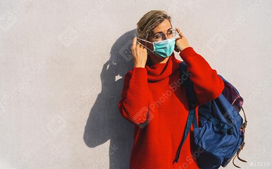 woman in round glasses takes off her turquoise face mask from her nose, dressed in a vibrant red sweater, with a distinct shadow behind her on a concrete wall  : Stock Photo or Stock Video Download rcfotostock photos, images and assets rcfotostock | RC Photo Stock.: