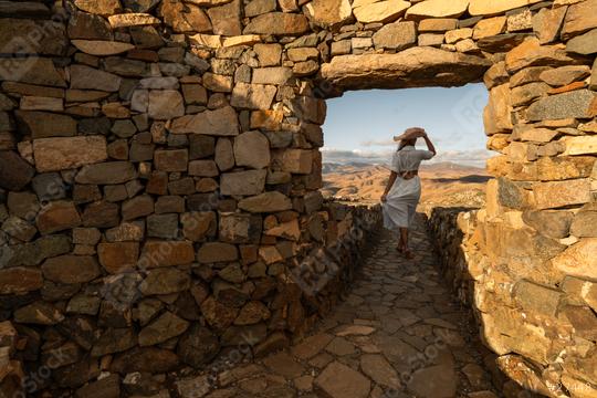 Woman in white dress and straw hat looking out from a stone archway at a mountainous landscape at fuerteventura   : Stock Photo or Stock Video Download rcfotostock photos, images and assets rcfotostock | RC Photo Stock.: