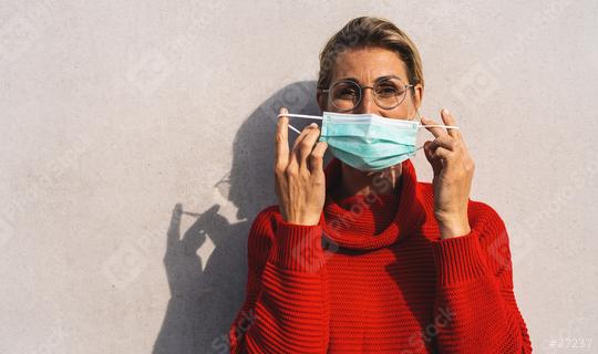 woman looks to camera in round glasses takes off her turquoise face mask from her nose, dressed in a vibrant red sweater, with a distinct shadow behind her on a concrete wall  : Stock Photo or Stock Video Download rcfotostock photos, images and assets rcfotostock | RC Photo Stock.: