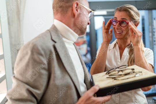 Woman trying on new glasses with optician holding a tray of eyewear in an optical store.  : Stock Photo or Stock Video Download rcfotostock photos, images and assets rcfotostock | RC Photo Stock.: