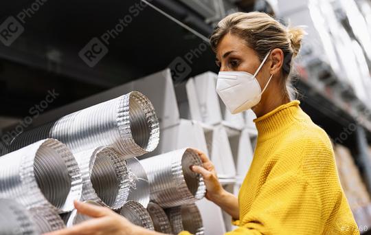 woman wearing a face mask and a yellow sweater examines silver ventilation ducts in a warehouse or store setting.  Corona safety Concept image  : Stock Photo or Stock Video Download rcfotostock photos, images and assets rcfotostock | RC Photo Stock.: