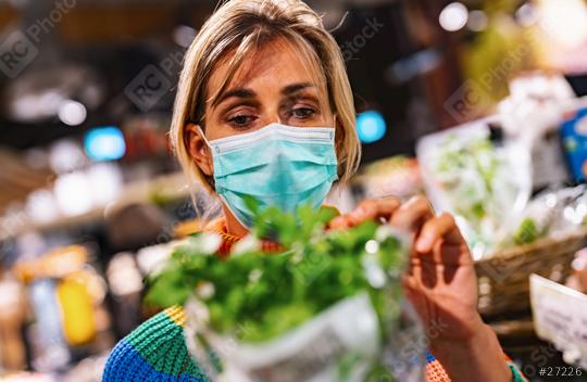 woman wearing a light blue face mask examines fresh basil in a bustling grocery store or supermarket, surrounded by an array of produce. Corona safety Concept image  : Stock Photo or Stock Video Download rcfotostock photos, images and assets rcfotostock | RC Photo Stock.: