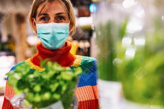 woman wearing a light blue face mask examines fresh basil in a bustling grocery store or supermarket, surrounded by an array of produce. Corona safety Concept image  : Stock Photo or Stock Video Download rcfotostock photos, images and assets rcfotostock | RC Photo Stock.: