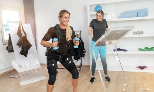 Woman with EMS training suit lifting dumbbells while trainer supervises with a tablet computer in a gym  : Stock Photo or Stock Video Download rcfotostock photos, images and assets rcfotostock | RC Photo Stock.: