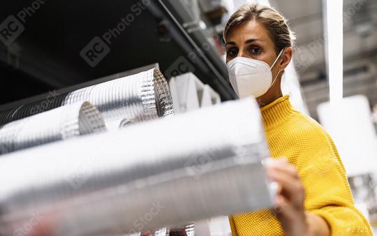 woman with face mask and a yellow sweater examines silver ventilation ducts in a warehouse or store setting. Corona safety Concept image  : Stock Photo or Stock Video Download rcfotostock photos, images and assets rcfotostock | RC Photo Stock.: