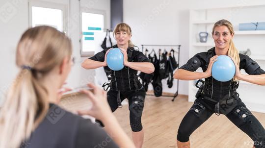 Women exercising with blue gym balls in front of a trainer in a training session and wearing EMS training suits at a EMS-Studio.  : Stock Photo or Stock Video Download rcfotostock photos, images and assets rcfotostock | RC Photo Stock.: