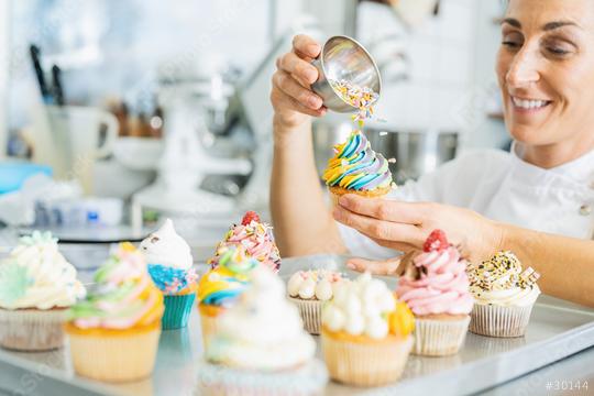 women in pastry bakery as confectioner sprinkles crumble mixture topping on a colorful muffin  by hand  : Stock Photo or Stock Video Download rcfotostock photos, images and assets rcfotostock | RC Photo Stock.: