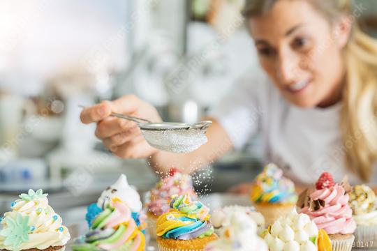 women in pastry bakery as confectioner sprinkles powdered sugar in a colander as topping on a colorful muffin  : Stock Photo or Stock Video Download rcfotostock photos, images and assets rcfotostock | RC Photo Stock.: