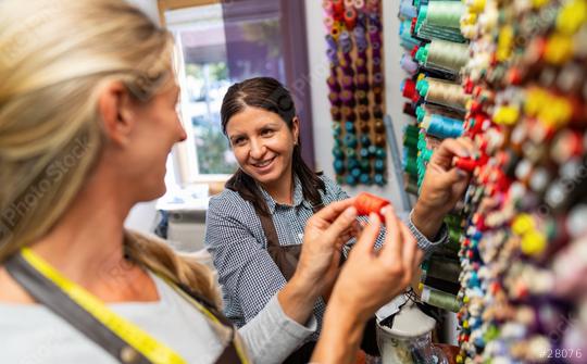 Work colleagues in a tailor shop, one in focus, share a moment in a sewing workspace. They