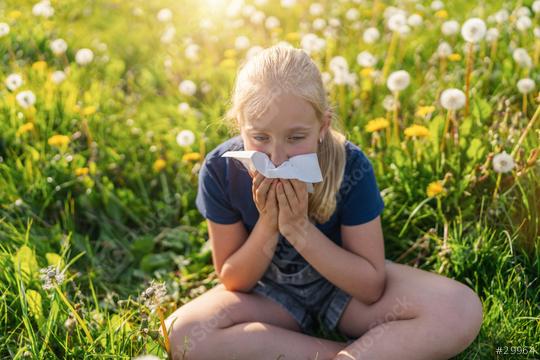 young girl sits in a field of dandelions, holding a handkerchief to her nose, showing signs of allergies. The bright sunlight and blooming flowers highlight the springtime setting.  : Stock Photo or Stock Video Download rcfotostock photos, images and assets rcfotostock | RC Photo Stock.: