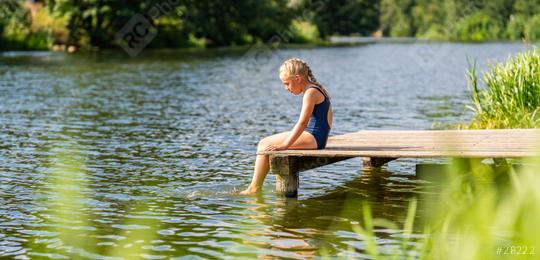 Young girl sitting alone on a wooden dock, dipping her feet in the lake on a sunny day at summer  : Stock Photo or Stock Video Download rcfotostock photos, images and assets rcfotostock | RC Photo Stock.: