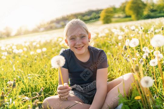 young girl sitting in a sunny field full of dandelions, holding one in her hand and smiling joyfully. The sun is shining brightly, capturing the essence of a warm and vibrant spring day.  : Stock Photo or Stock Video Download rcfotostock photos, images and assets rcfotostock | RC Photo Stock.: