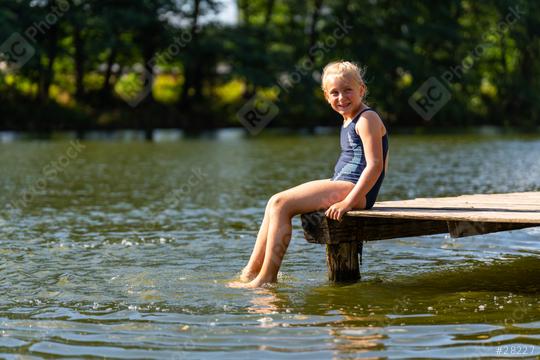 Young girl sitting on a wooden dock, smiling and dangling her feet in the lake on a sunny day in germany  : Stock Photo or Stock Video Download rcfotostock photos, images and assets rcfotostock | RC Photo Stock.: