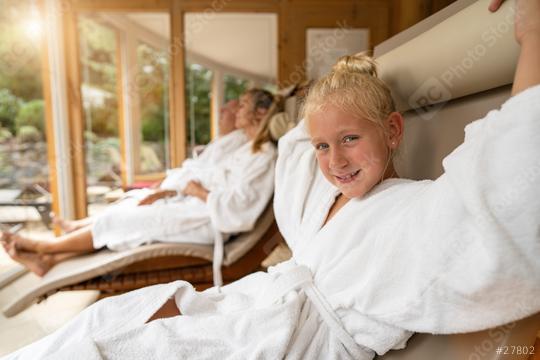 young girl smiling in the foreground, with her family relaxing in robes in the background, in a bright spa hotel lounge  : Stock Photo or Stock Video Download rcfotostock photos, images and assets rcfotostock | RC Photo Stock.: