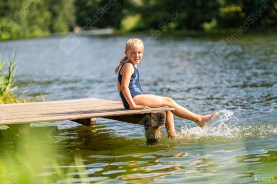 Young girl smiling to camera and kicking water while sitting on a wooden dock by a lake on a bright day at summer  : Stock Photo or Stock Video Download rcfotostock photos, images and assets rcfotostock | RC Photo Stock.: