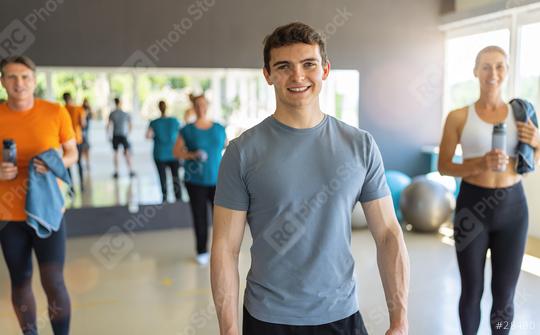 Young man in grey t-shirt smiling in a gym with other people in the background. Teamwork Concept image  : Stock Photo or Stock Video Download rcfotostock photos, images and assets rcfotostock | RC Photo Stock.: