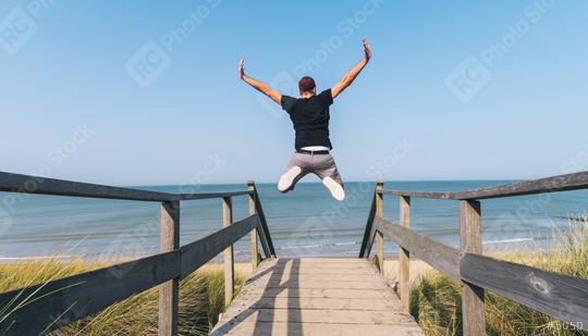 Young Man Jumps on Beach over a wooden path to the Baltic sea on a summer day  : Stock Photo or Stock Video Download rcfotostock photos, images and assets rcfotostock | RC Photo Stock.: