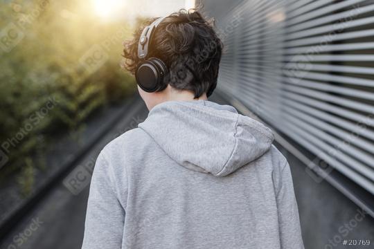 Young person from behind wears headphones. An adult man listens to music on the street in an urban space at sunset.   : Stock Photo or Stock Video Download rcfotostock photos, images and assets rcfotostock | RC Photo Stock.: