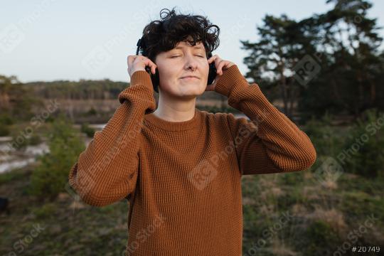 Young person with closed eyes listens to music with headphones in nature. The relaxed person enjoys the song and enjoys life.  : Stock Photo or Stock Video Download rcfotostock photos, images and assets rcfotostock | RC Photo Stock.: